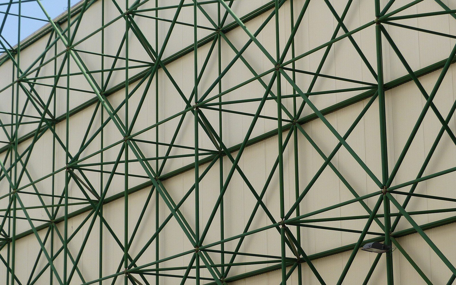 Green diagonal steel trusses form a crisscross pattern against a building's beige wall