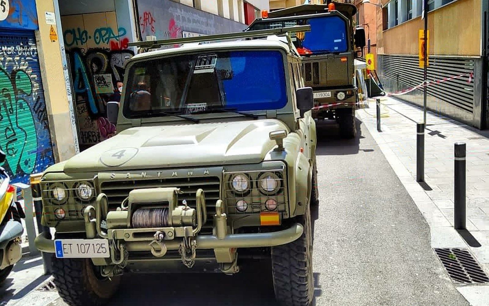 Military Santana Land Rover and truck parked on a narrow graffiti-lined street