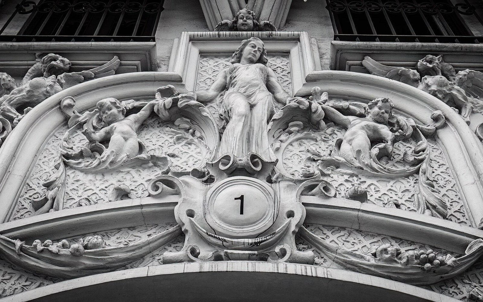 Ornate stone facade carving with cherubs and a female figure above the number one